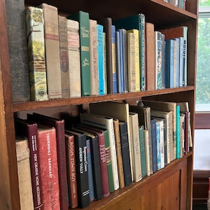 May include: A wooden bookshelf filled with a variety of vintage books. The books have different colors, sizes, and cover designs. Some titles visible include "The Road to Safety" and "Boom Town Boy". The bookshelf is made of dark wood.
