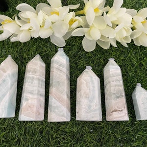 May include: Seven polished blue calcite crystal points of varying sizes, arranged on a green grassy surface.