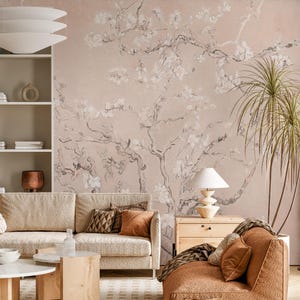 Puede incluir: Un interior de sala de estar con un mural de pared rosa claro que presenta una pintura estilizada de un árbol en flor con flores blancas. El mural es una opción de diseño popular para la decoración del hogar.