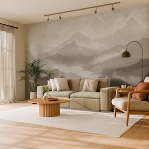 May include: A contemporary living room featuring a muted colour scheme. A beige sofa with cushions is positioned before a mountain mural. A wooden coffee table and armchair are present, along with a large rug and a potted plant.