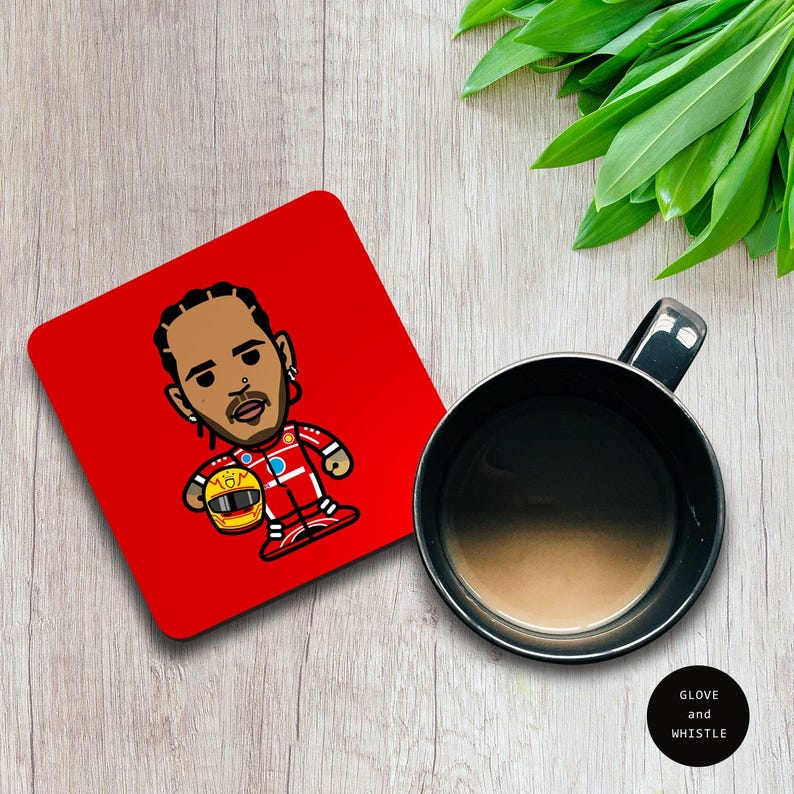 May include: Red square coaster with a cartoon illustration of a Formula 1 driver wearing a red racing suit and helmet. The driver is holding a yellow helmet in his left hand. The coaster is on a wooden surface.