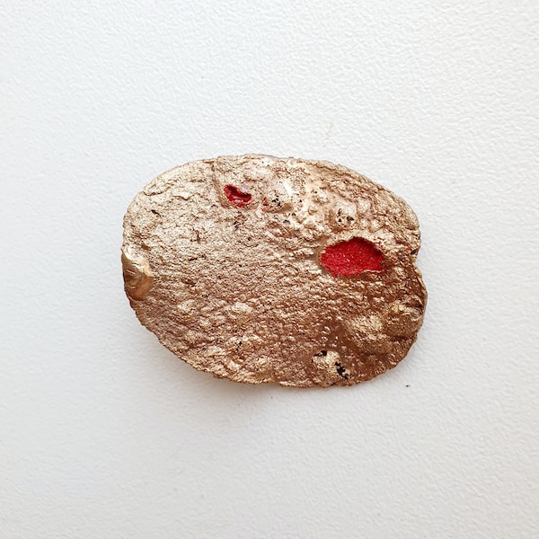 Broche de bronce de textura rugosa y un punto de esmalte rojo