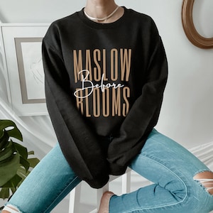 May include: Black sweatshirt with the text "MASLOW Before BLOOMS" in brown lettering.