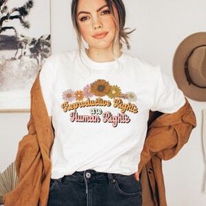 Puede incluir: Camiseta blanca con un dise&ntilde;o floral y el texto "Reproductive Rights are Human Rights" en una fuente retro.