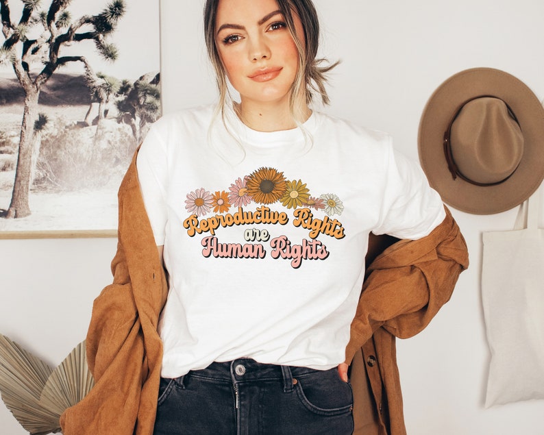 Puede incluir: Camiseta blanca con un dise&ntilde;o floral y el texto "Reproductive Rights are Human Rights" en una fuente retro.