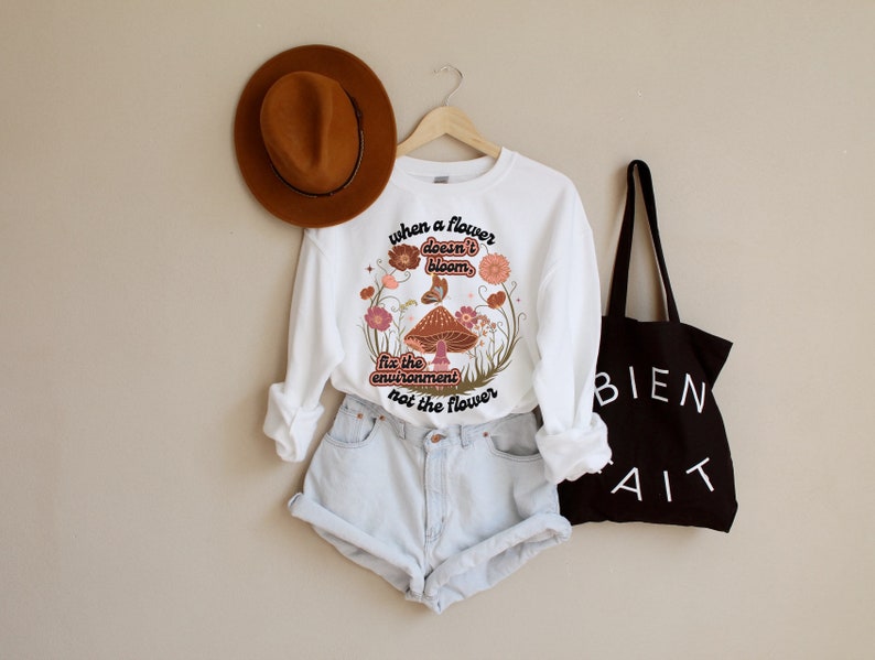 K&ouml;nnte beinhalten: Wei&szlig;er Langarm-Pullover mit einem Pilz-Motiv und dem Text "Wenn eine Blume nicht bl&uuml;ht, repariere die Umwelt, nicht die Blume".