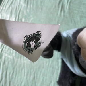 Op de afbeelding: Een witte patch met een groen logo waarop "Carolina Tar Heels" staat met een tekening van een rammenkop erin. Het logo bevindt zich op een zwart en blauw pluche speelgoed.