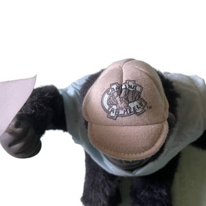 Op de afbeelding: Een zwarte en blauwe pluche gorilla die een beige baseballpet draagt met de tekst "Carolina Tar Heels" geborduurd op de voorkant.