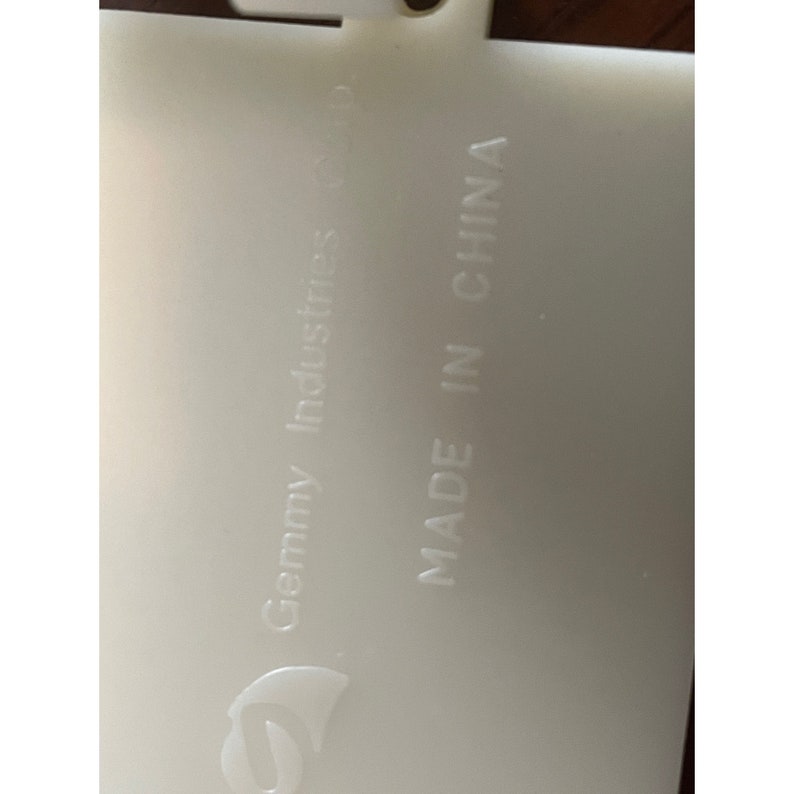 Op de afbeelding: Wit plastic label met de tekst "Gemmy Industries" en "MADE IN CHINA" erop gegraveerd.