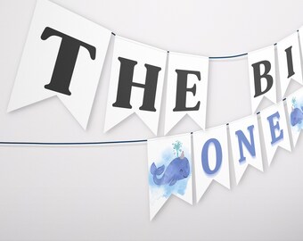 May include: A white banner with blue and black lettering that reads "The Big One" with a blue whale illustration on the "One" flag.