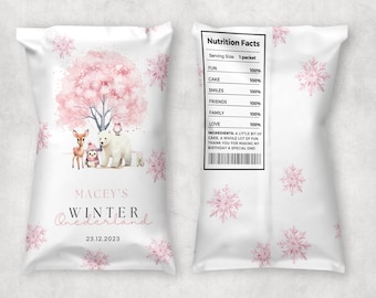 May include: A white and pink party favor bag with a winter wonderland theme. The bag features a pink and white snowflake design, a pink cherry blossom tree, a polar bear, a deer, and a penguin. The bag also includes the text "Macey's Winter Wonderland" and the date "23.12.2023".