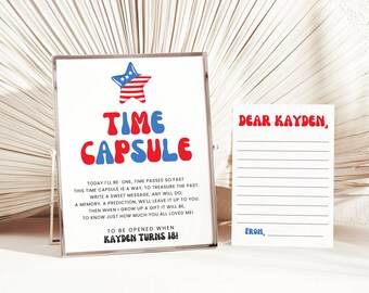 Op de afbeelding: Een witte kaart met rode en blauwe tekst die "Tijdcapsule" zegt met een rode, witte en blauwe ster boven de tekst. De kaart bevat ook instructies voor het maken van een tijdcapsule die geopend moet worden wanneer iemand 18 jaar wordt. Een witte kaart met rode en blauwe tekst die "Beste Kayden, Van," zegt, staat naast de tijdcapsulekaart.