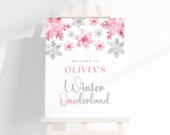 May include: Welcome to Olivia's Winter Wonderland sign with pink and grey watercolour snowflakes. The sign is white with black text.