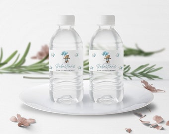 May include: Two clear plastic water bottles with blue and white labels. The labels feature a cartoon bear holding blue balloons and the text "Sebastian's Bear-y First Birthday".
