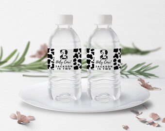 May include: Two clear plastic water bottles with black and white cow print labels. The labels say "Holy Cow! Jackson is Two".