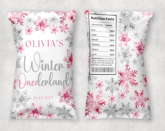 May include: A white favor bag with a pink and gray snowflake pattern. The bag says "Olivia's Winter Onederland" and "24.12.2023". The back of the bag has a nutrition facts label with a list of fun things like cake, smiles, and friends.