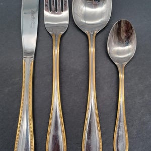 May include: A set of four silver-plated cutlery pieces with gold accents. The set includes a knife, fork, tablespoon, and teaspoon.