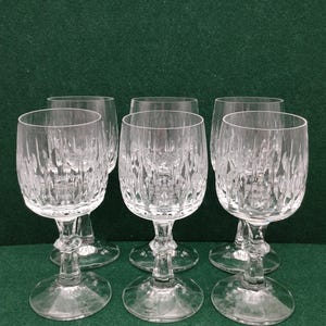 Op de afbeelding: Zes heldere kristallen wijnglazen met een getextureerd, geslepen glazen ontwerp. De glazen hebben een afgeronde kom, een steel en een cirkelvormige voet. De glazen staan op een groene ondergrond.