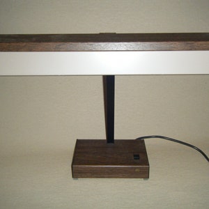 May include: A vintage wooden desk lamp with a black metal arm and a white light panel. The lamp has a brown wooden base with a power switch.