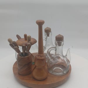 Könnte beinhalten: Ein hölzernes Servierset auf einem runden Tablett. Es enthält kleine Glasflaschen mit Korken, einen Salzstreuer, eine Pfeffermühle und einen Behälter mit kleinen Gabeln. Das Set besteht aus Holz und Glas.