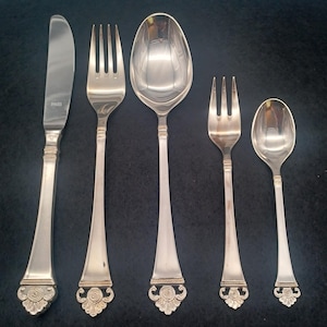 Peut inclure: Un ensemble de cinq couverts en argent plaqué avec des poignées ornées. L'ensemble comprend un couteau, deux fourchettes et deux cuillères.