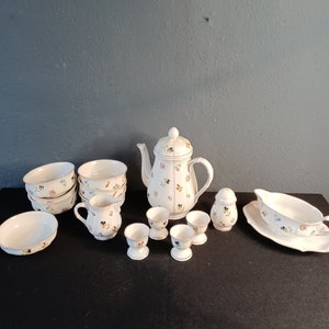 Peut inclure: Un ensemble de vaisselle en porcelaine blanche avec un motif floral. L'ensemble comprend une théière, un pot à crème, un sucrier, quatre bols, quatre coquetiers et une saucière.