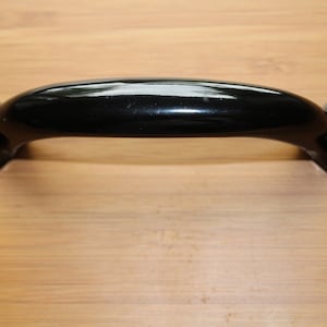 May include: Black metal door handle with a curved design and two holes on each side.