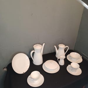 Könnte beinhalten: Ein weißes Porzellan-Tee-Set mit einer Teekanne, einer Milchkännchen, einer Zuckerdose und vier Tassen und Untertassen.