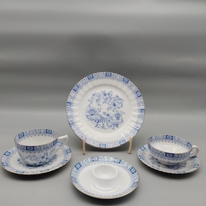 Könnte beinhalten: Vintage Porzellan-Teeservice mit blau-weißem Blumenmuster. Das Set beinhaltet zwei Teetassen mit Untertassen, einen Servierteller und einen Eierbecher. Die Teller und Tassen haben einen gewellten Rand und einen goldenen Rand.