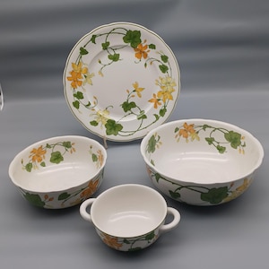 Puede incluir: Un juego de vajilla de cerámica blanca con un diseño floral de flores amarillas y naranjas y hojas verdes. El juego incluye un plato, dos cuencos y una taza con asa.