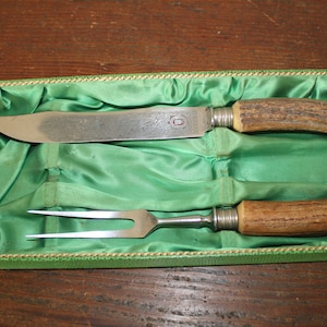 May include: A set of two silver-toned hunting knives with antler handles, in a green velvet lined box.