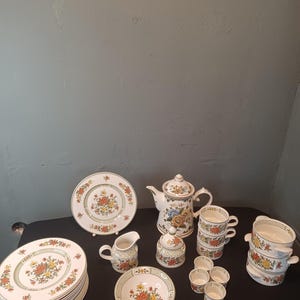 Puede incluir: Un juego de té floral vintage completo, que incluye platos, tazas, una tetera, una crema, un azucarero y cuencos pequeños. El juego presenta un fondo blanco con un diseño floral colorido.