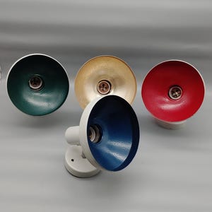 Pode incluir: Quatro candeeiros de parede com bases brancas e abajures circulares. O interior de cada abajur apresenta uma cor distinta: verde escuro, dourado, vermelho e azul. Cada candeeiro tem um casquilho central visível dentro do abajur.
