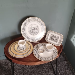 Puede incluir: Una bandeja de madera con patas de metal negro contiene un juego de cuatro platos y una taza. Los platos tienen un patrón floral blanco y negro con un borde amarillo. La taza es blanca con un patrón floral blanco y negro.