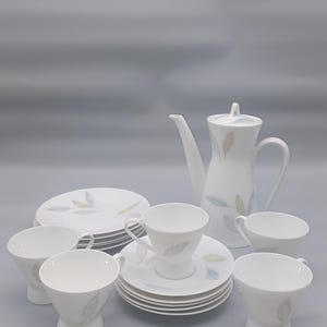 Puede incluir: Juego de té de porcelana blanca con diseño de hojas. El juego incluye una tetera, tazas, platillos y platos. El diseño de hojas presenta detalles en azul, amarillo y gris. Ideal para servir té o café.