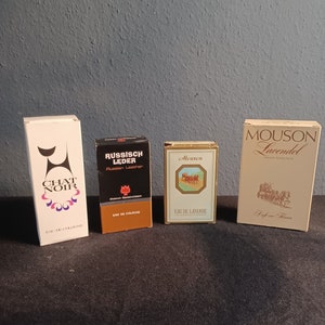 May include: Four cologne bottles with gold accents. The bottles are labelled "Chat Noir", "Russisch Leder", "Mouson", and "Mouson Lavendel".