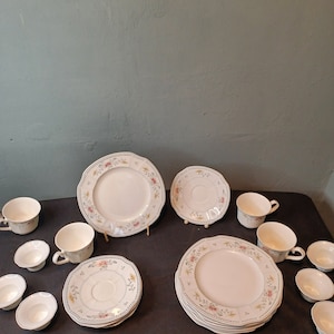 May include: A set of white floral patterned dinnerware, including plates, saucers, and cups. The set features a delicate floral design with pink, yellow, and green accents.