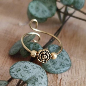 Könnte beinhalten: Ein verstellbarer Ring aus Gold mit einem dekorativen Rosenmotiv. Der Ring ist aus Draht gefertigt und hat einen Perlenakzent.