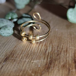 Könnte beinhalten: Ein goldener Ring mit einem doppelten Band und vier kleinen goldenen Perlen. Der Ring liegt auf einer Holzoberfläche.