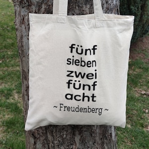 Könnte beinhalten: Eine weiße Stofftasche mit schwarzem Text, der "fünf sieben zwei fünf acht ~ Freudenberg ~" lautet.