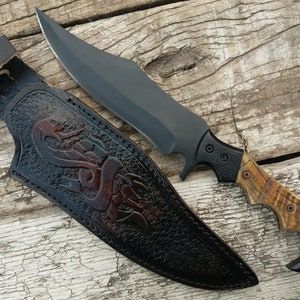 May include: A black and brown hunting knife with a leather sheath. The sheath has a decorative snake design. The knife has a black handle with a brown wood inlay.