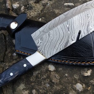 May include: A black-handled knife with a damascus steel blade and a black leather sheath. The blade has a wavy pattern and a serrated edge.