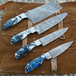May include: Set of four kitchen knives with blue and white patterned handles. The knives are arranged on a brown leather roll with a yellow stitching detail.