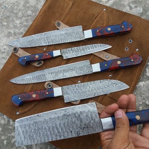 May include: Set of five kitchen knives with blue and red patterned handles. The knives have a Damascus steel blade with a wavy pattern. The knives are displayed on a brown leather roll.