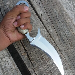 May include: A silver-colored knife with a curved blade and a bone handle. The knife has a ring on the handle for easy grip.