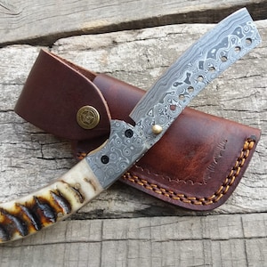 Peut inclure: Un rasoir droit avec une lame en acier à motifs et un étui en cuir marron. Le manche est en matériau brun clair avec un motif brun foncé.