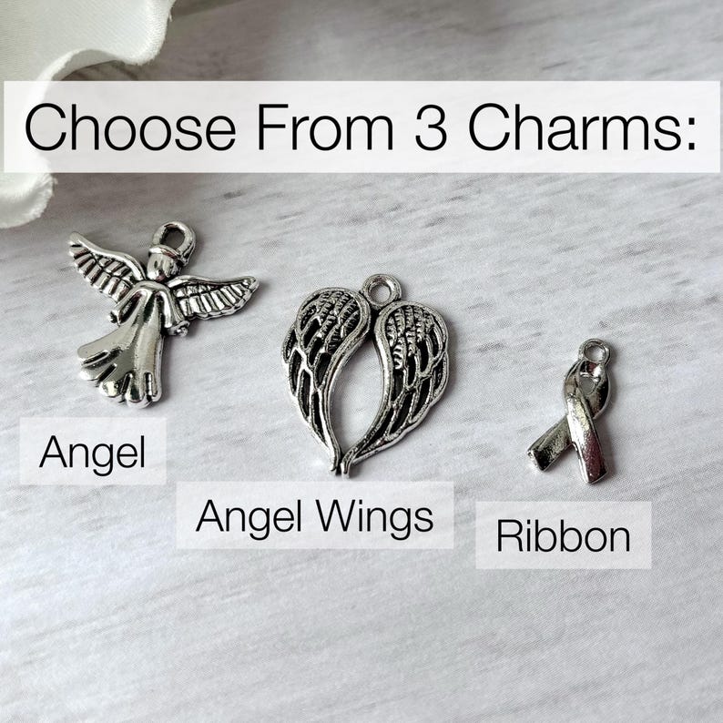 May include: Three silver-toned metal charms featuring an angel, a pair of angel wings, and a ribbon. The text "Choose From 3 Charms:" appears at the top, with labels "Angel," "Angel Wings," and "Ribbon" positioned below each respective charm.