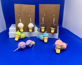 May include: A set of six pairs of ice cream cone earrings. The earrings are made of polymer clay and feature different flavors of ice cream, including chocolate, vanilla, strawberry, mint chip, and cookie dough. The earrings are all on silver hooks.