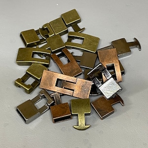 May include: A pile of metal clasps in various finishes, including silver, gold, and copper. The clasps are rectangular and have a simple design.