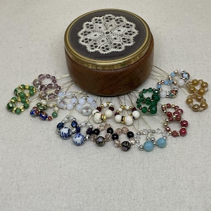 Könnte beinhalten: Eine Holzschmuckschatulle mit einem Spitzendesign auf dem Deckel ist von verschiedenen Perlenringen umgeben. Die Ringe weisen eine Vielzahl von Farben und Perlenarten auf, darunter Grün, Lila und Blau.